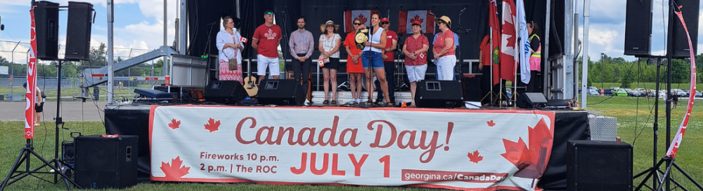 People standing on stage with a Canada Day banner hanging below them