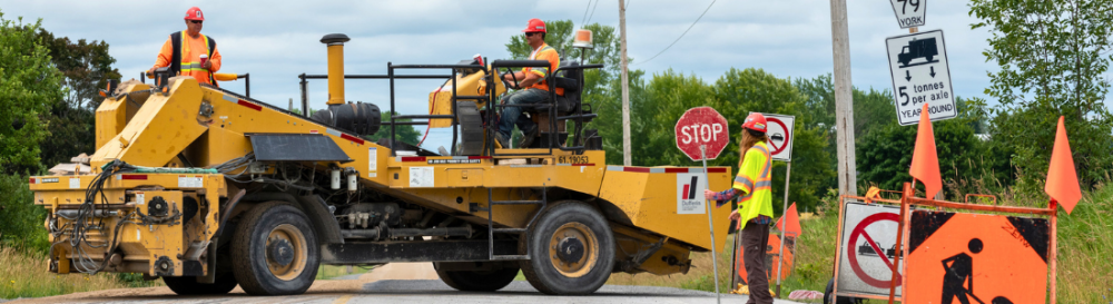 A piece of construction equipment blocking the road and person holding a stop sign