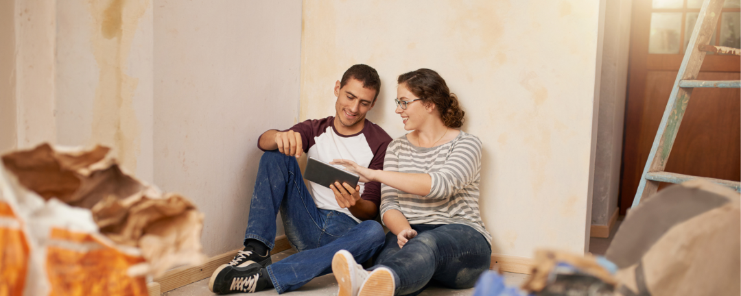 man and woman sitting on the floor of a home under renovation looking at a tablet